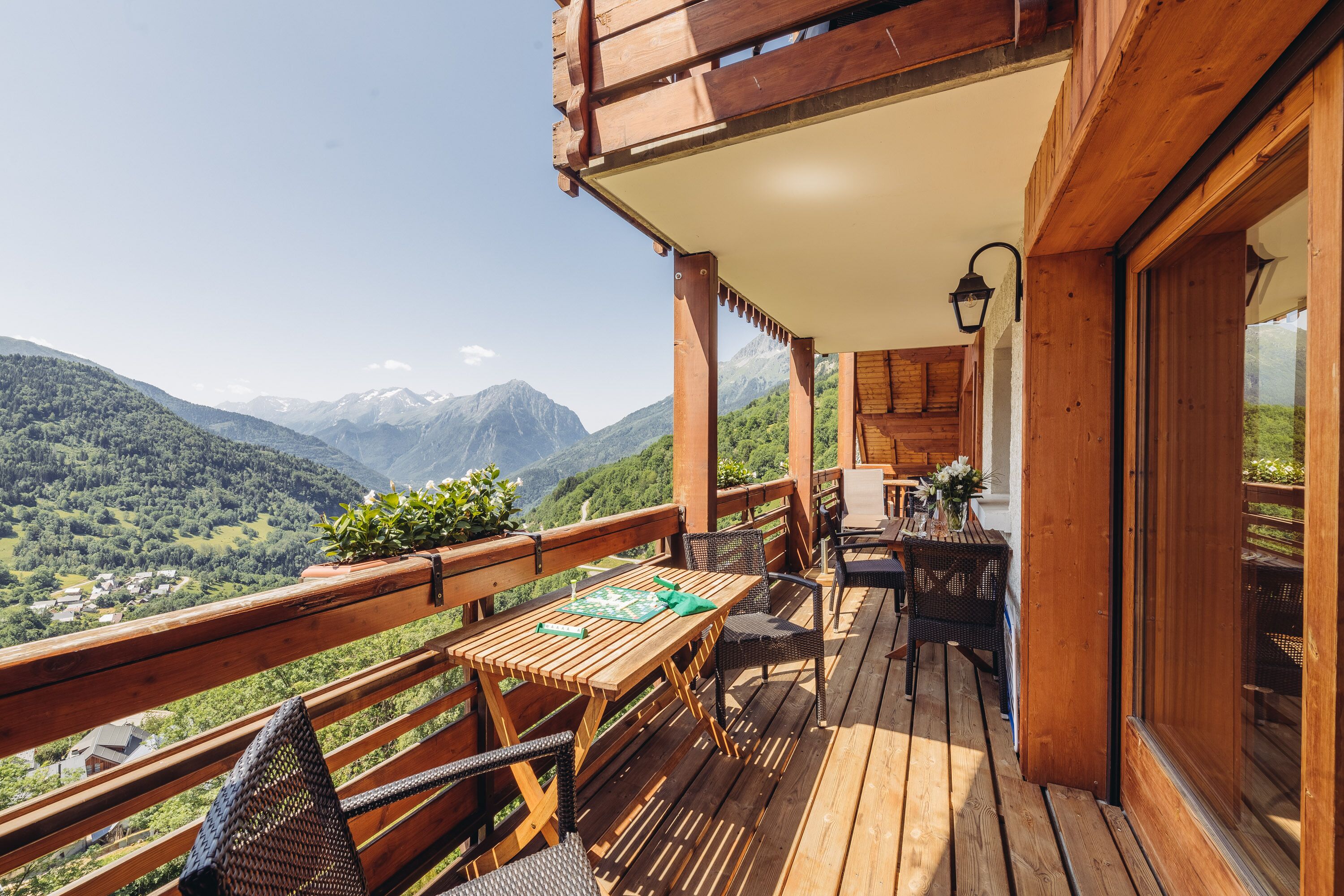 A wooden deck with a table and chairs, overlooking a mountainous landscape.