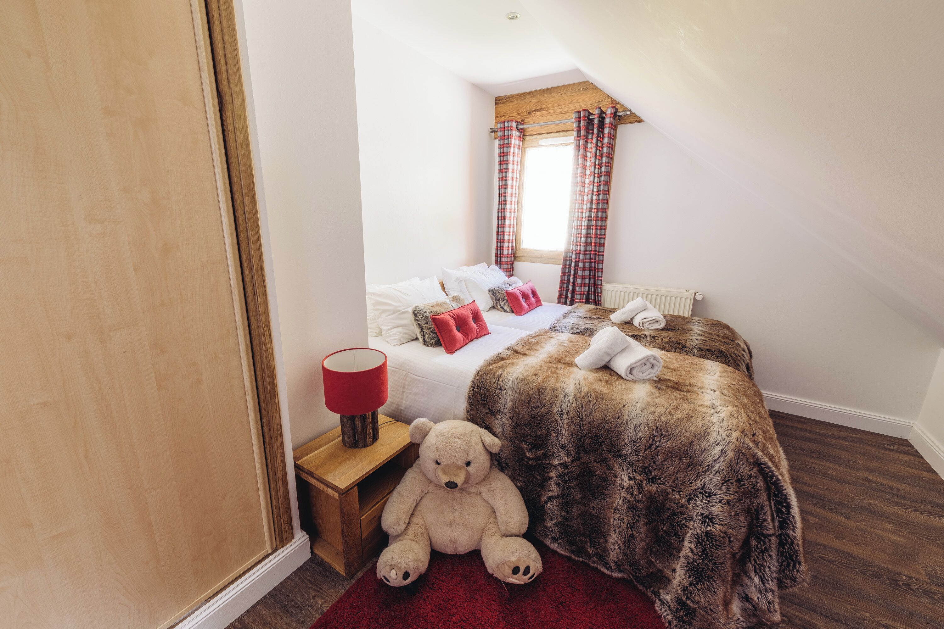 A bedroom with a bed, a teddy bear, a red lamp, and a window with curtains.