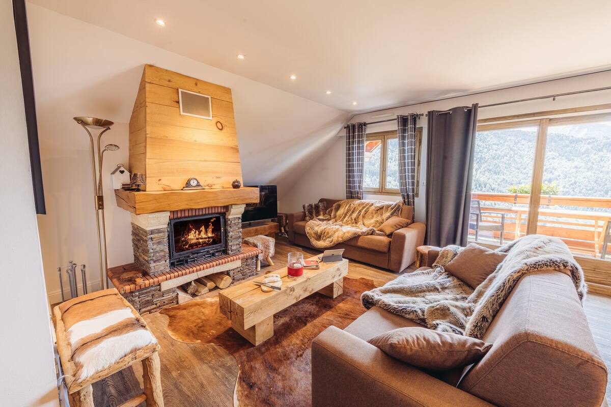 A cozy living room with a fireplace, comfortable seating, and a view of the outdoors.