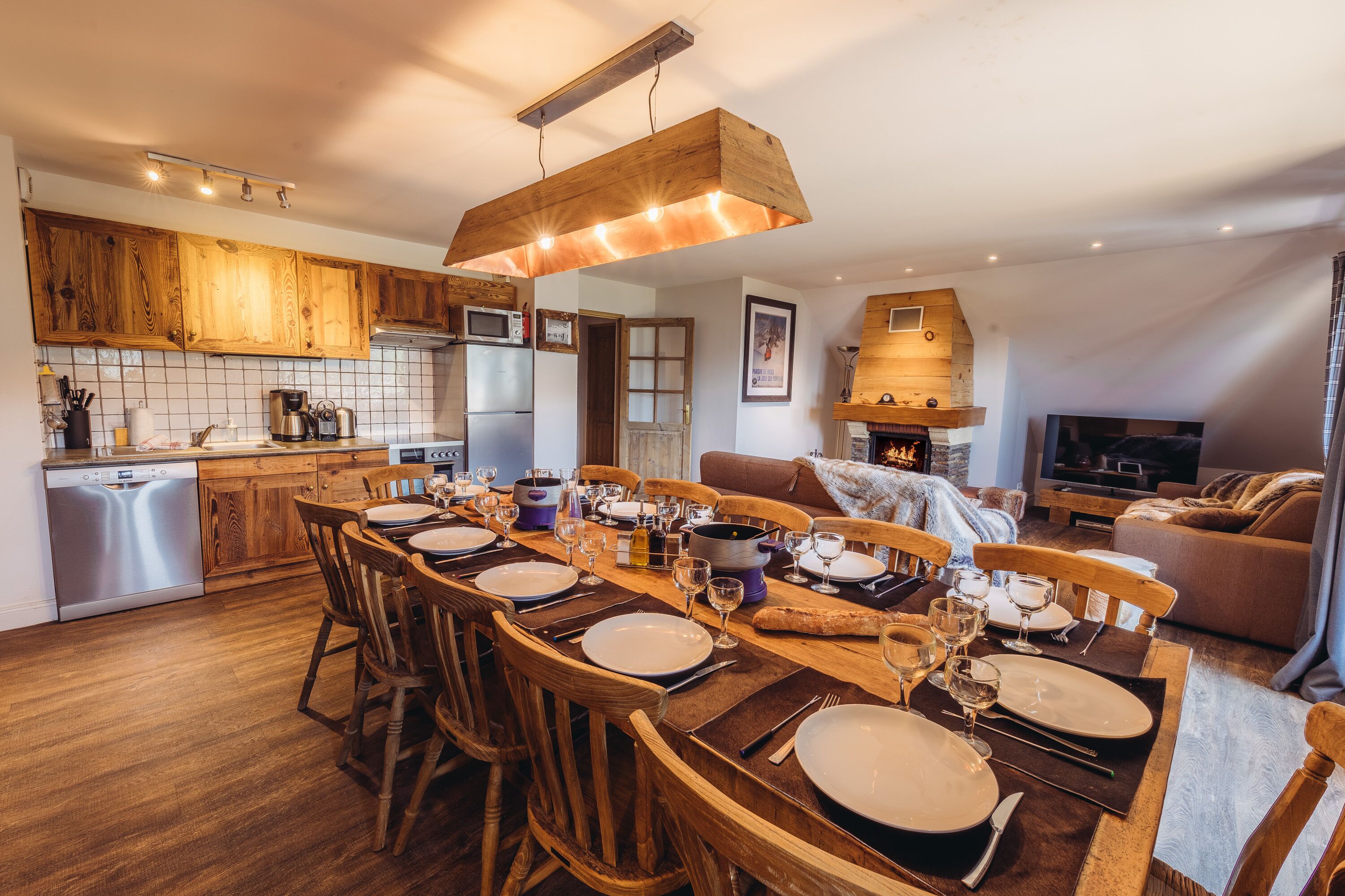 A modern kitchen with wooden cabinets, a dining area set for six, and a cozy living space with a fireplace.