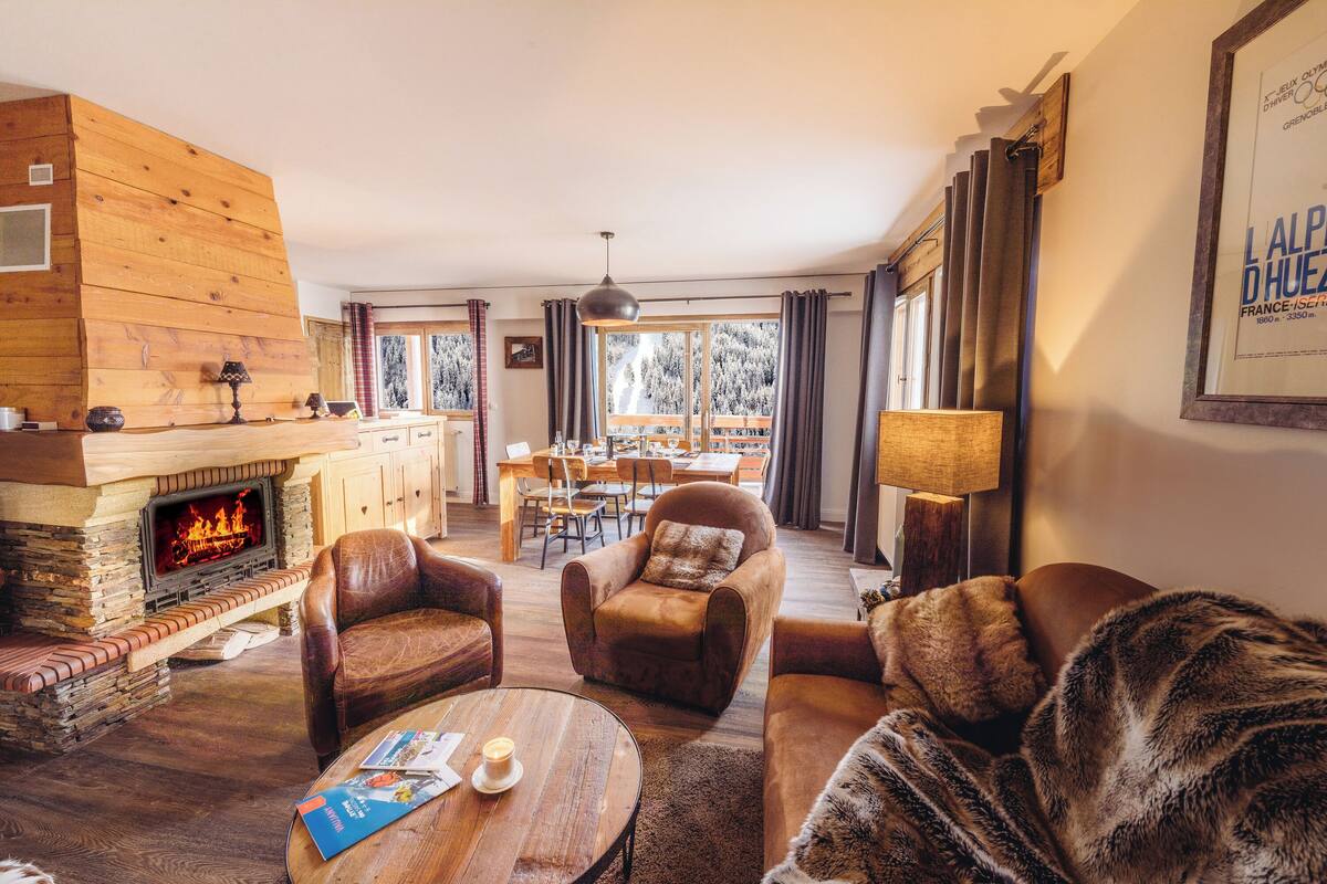 A cozy living room with a fireplace, leather sofas, a dining area, and a view of a snowy landscape.