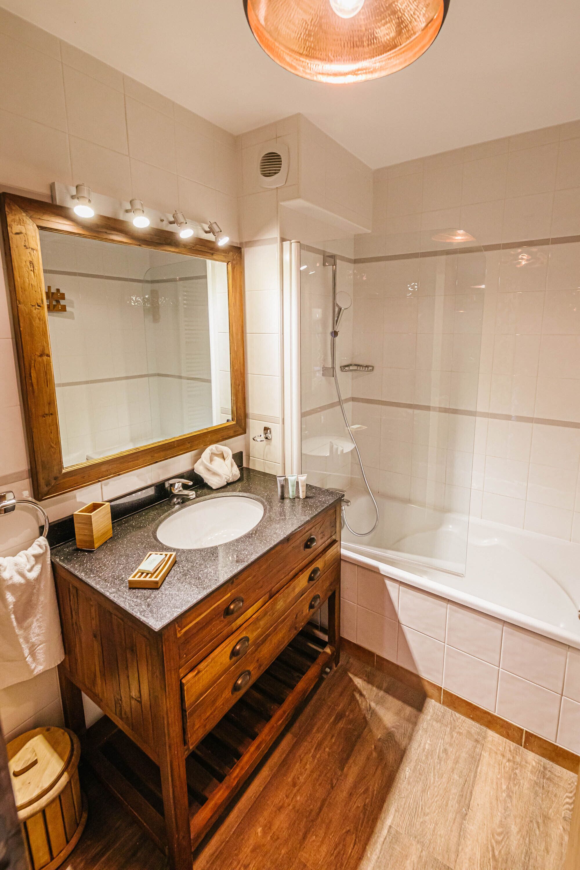 Une salle de bain avec un meuble-lavabo en bois, un grand miroir, un lavabo, une douche et une baignoire.