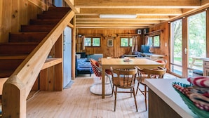 A cabin interior with a wooden staircase, a dining area with a table and chairs, a kitchen with a stove, and large windows providing natural light. - Domaine de la Poignardiere (Chatillon-sur-Indre)