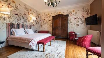 A bedroom with a bed, bench, red polka dot chairs, a small table, and a TV.
