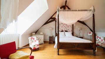 Une chambre à coucher avec un lit à baldaquin, un fauteuil rouge, une petite table de chevet et une fenêtre avec des rideaux.
