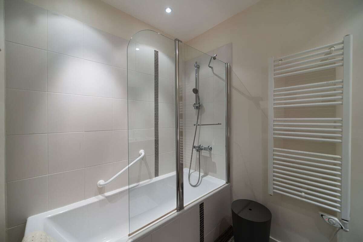 A modern bathroom with a glass-enclosed shower, a white bathtub, and a white towel rack.