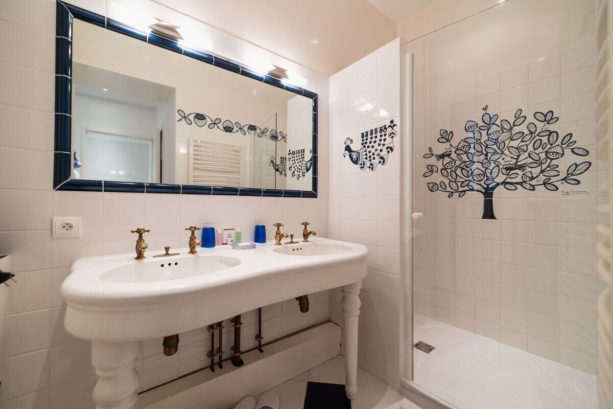 Une salle de bain avec deux lavabos, un grand miroir et des œuvres d’art décoratives au mur.
