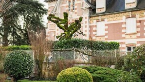 A building with a prominent tower and a well-maintained garden with various shrubs and a neatly trimmed bush. - Domaine de la Poignardiere (Chatillon-sur-Indre)