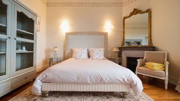 Une chambre à coucher avec un grand lit, une commode, une chaise, un miroir et une cheminée.