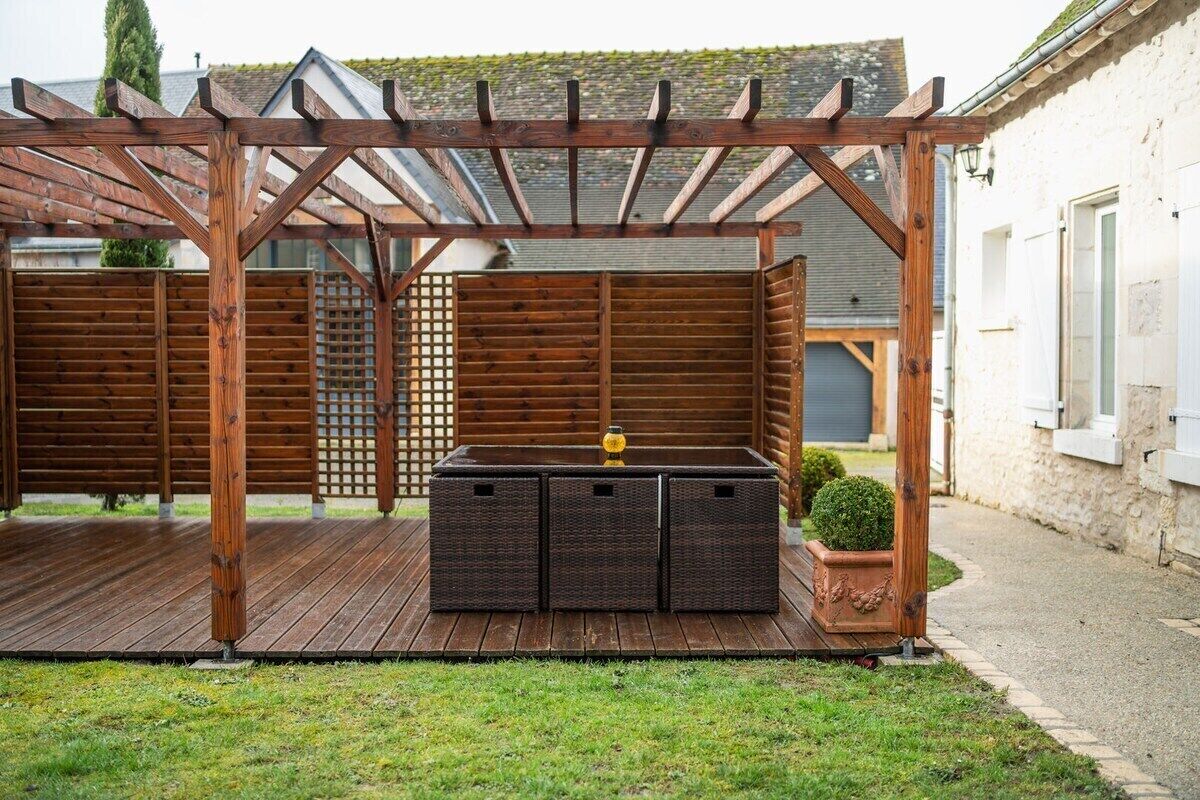 Una pérgola de madera con zona de estar integrada y una pequeña planta en maceta.