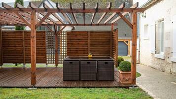 Una pérgola de madera con zona de estar integrada y una pequeña planta en maceta.