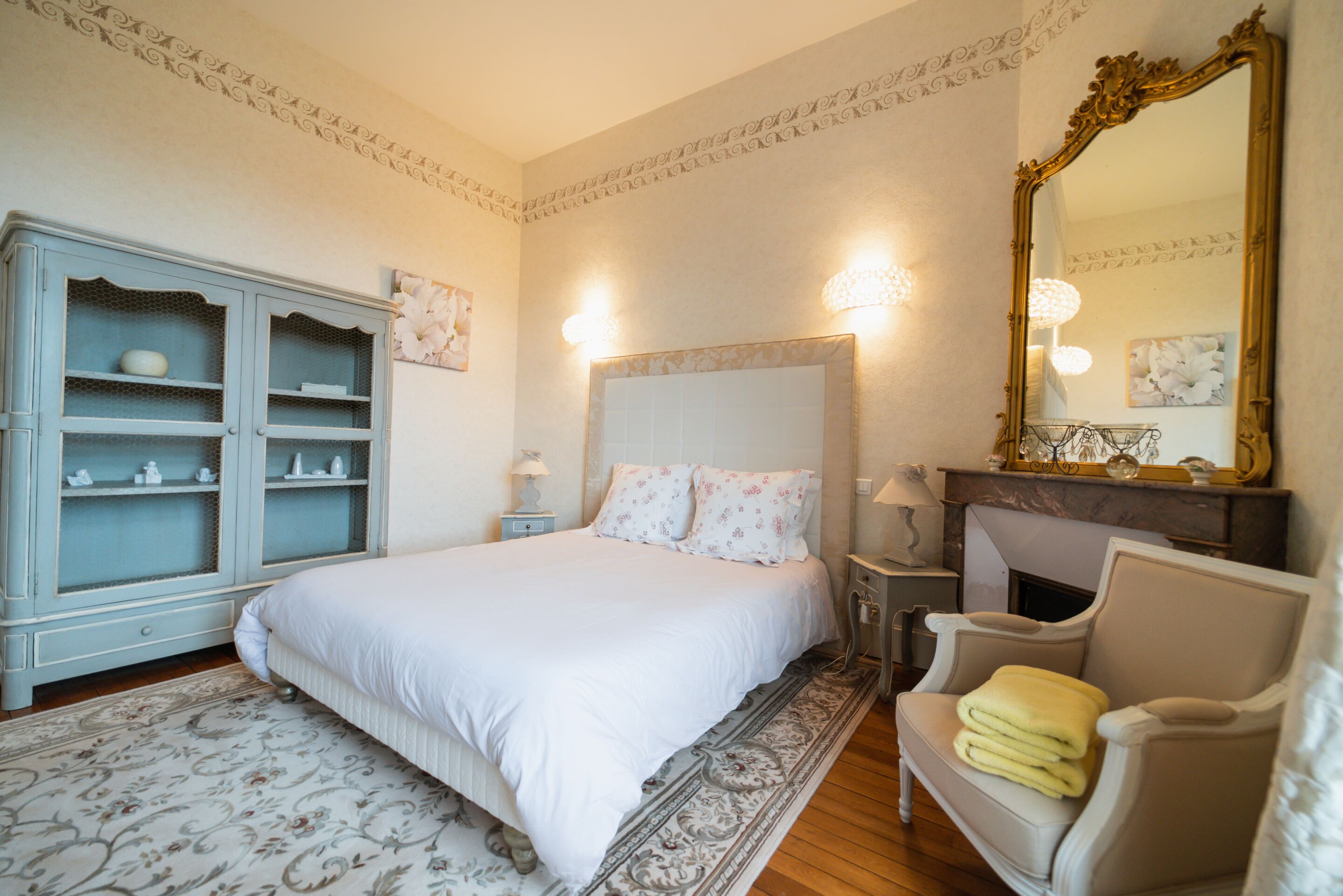 A bedroom with a large bed, a dresser, a chair, a fireplace, and a mirror.