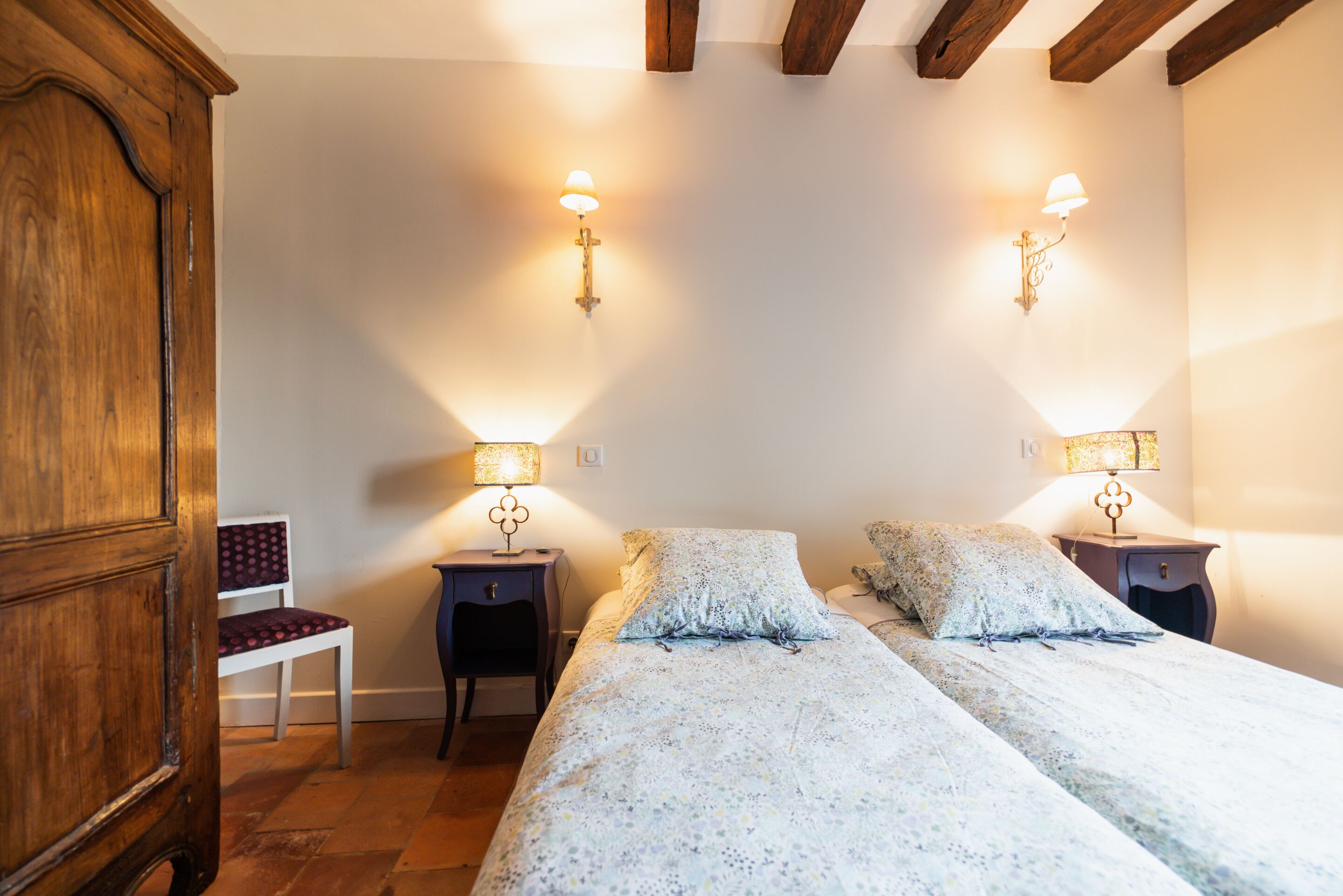 Una camera da letto con due letti, un armadio in legno, una sedia e lampade a parete.
