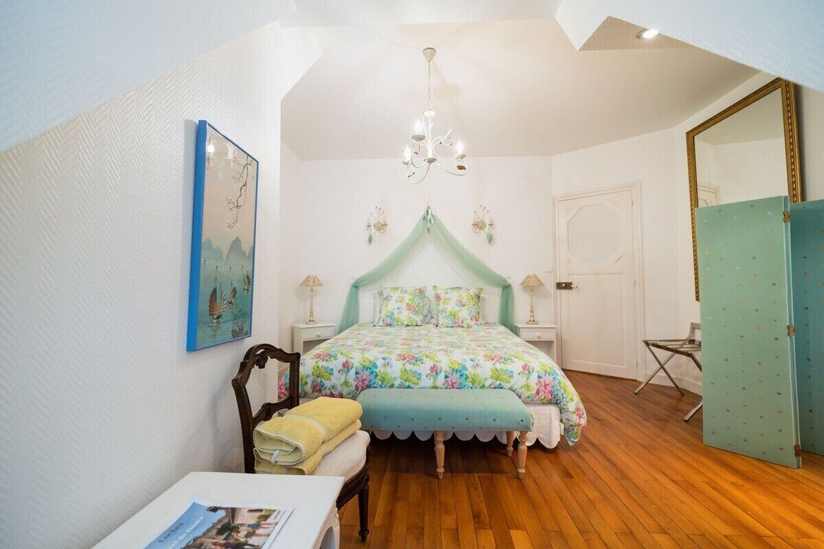 A bedroom with a bed, a chair, a table, a mirror, and a door.