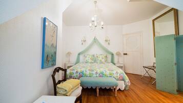 A bedroom with a bed, a chair, a table, a mirror, and a door.
