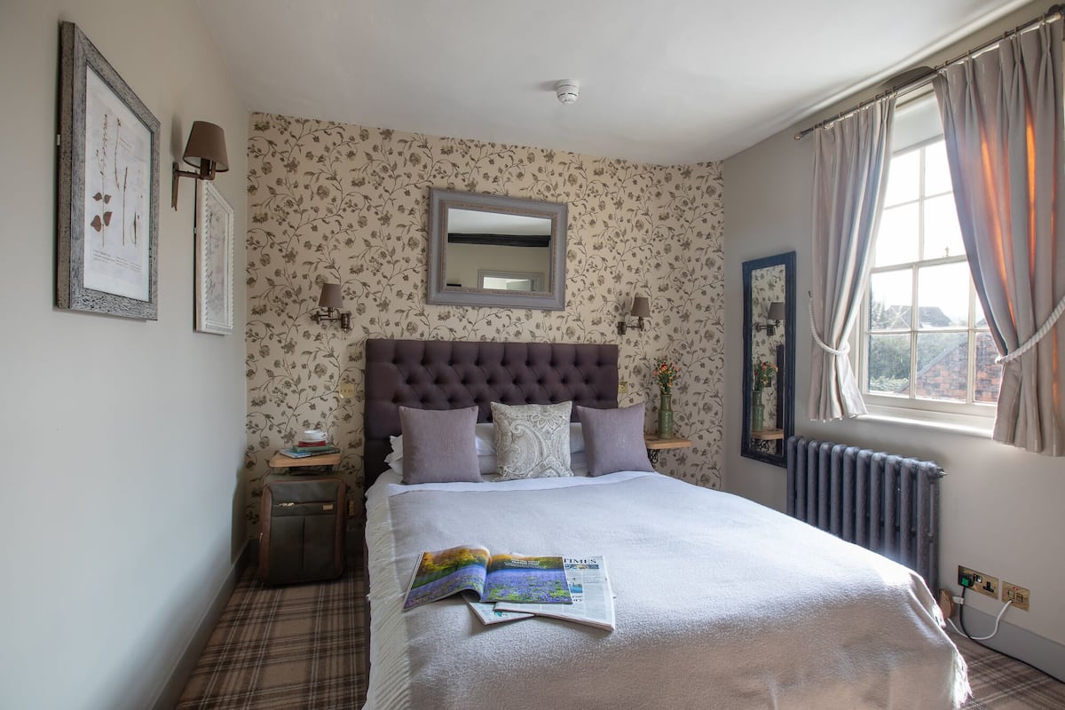 A neatly arranged bedroom with a large bed, a bedside table, a mirror, and a window with curtains.