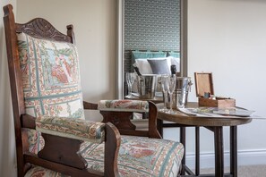 A traditional wooden chair with a patterned cushion, a small round table with a tray, and a window with a floral pattern. - The Running Horses (Dorking)