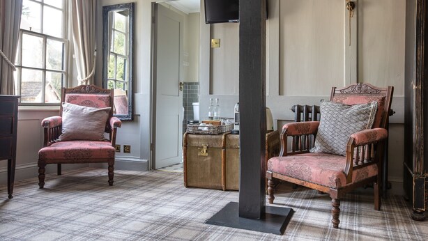 A room with two vintage-style chairs, a large mirror, a television, and a radiator. - The Running Horses (Dorking)