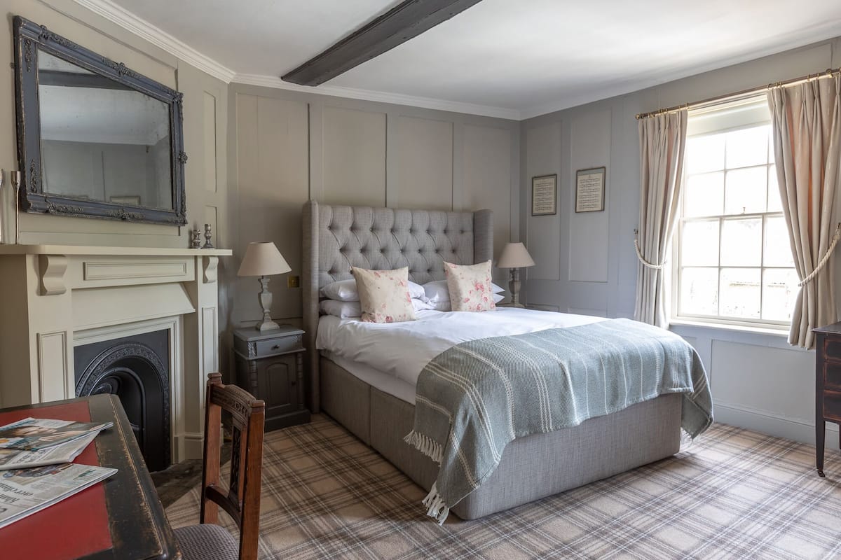 A bedroom with a large bed, a fireplace, a mirror, and a window with curtains.