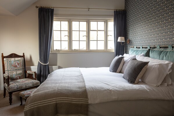 A bedroom with a large bed, a chair, a window with curtains, and a patterned wall.