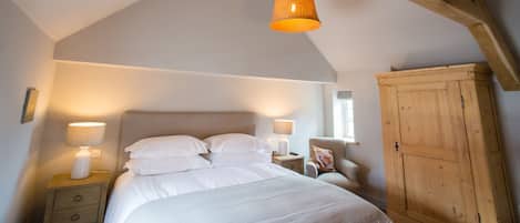 Un dormitorio con una cama grande, dos lámparas de noche, un armario de madera y vigas de madera a la vista en el techo.