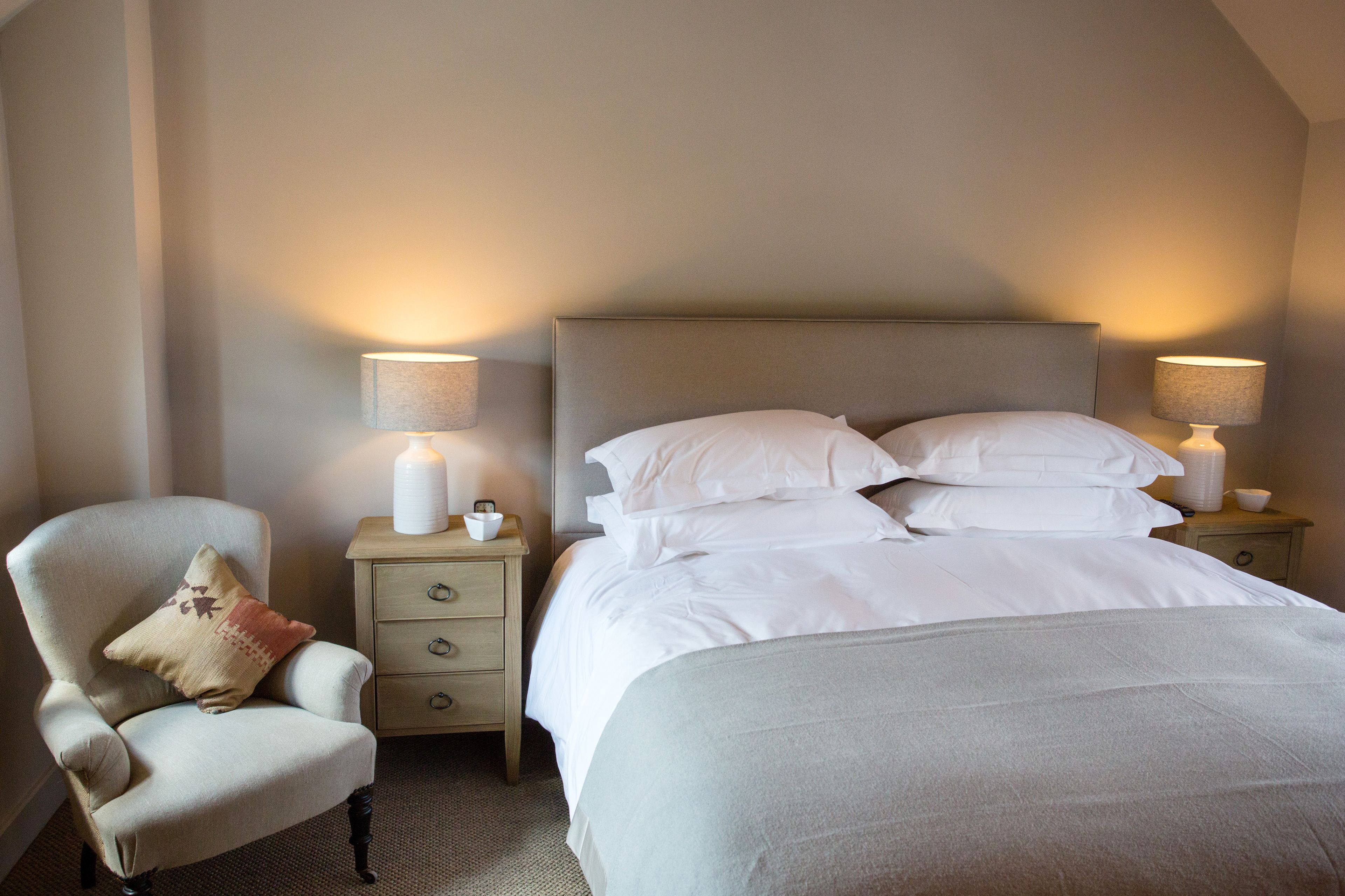 A neatly arranged bedroom with a large bed, two bedside tables with lamps, a chair, and a nightstand.
