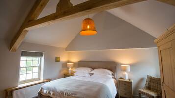 Een slaapkamer met een groot bed, twee nachtkastjes, een stoel, een raam en houten balken in het plafond.
