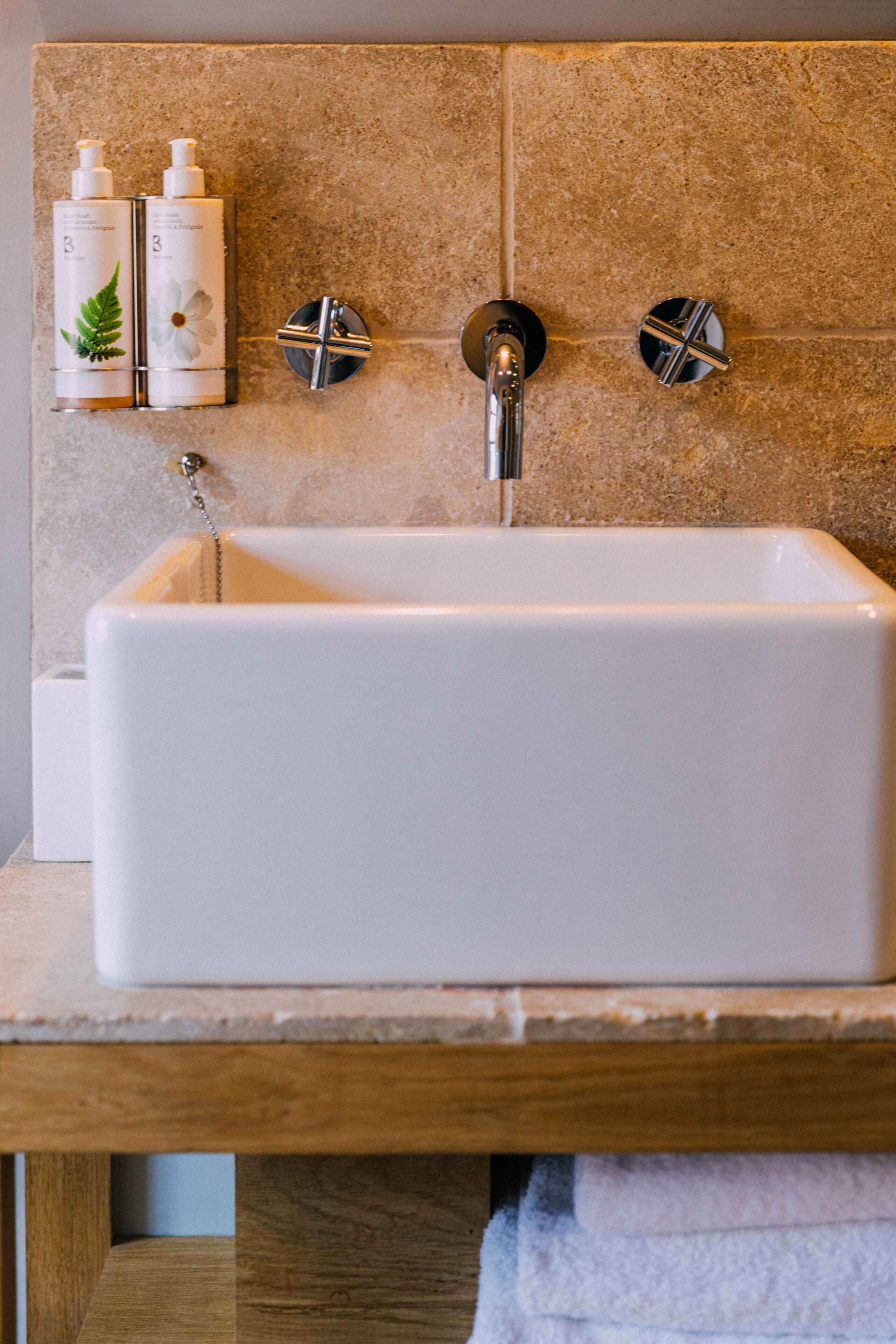 Een badkamer met een rechthoekig wastafelblad, twee kraanwerkens en twee zeepdispensers op een beigekleurde betegelde muur.