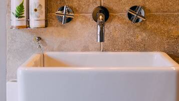 Een badkamer met een rechthoekig wastafelblad, twee kraanwerkens en twee zeepdispensers op een beigekleurde betegelde muur.