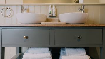 Un baño con dos lavamanos tipo recipiente, un perchero y un espejo sobre un mueble gris con dos cajones.