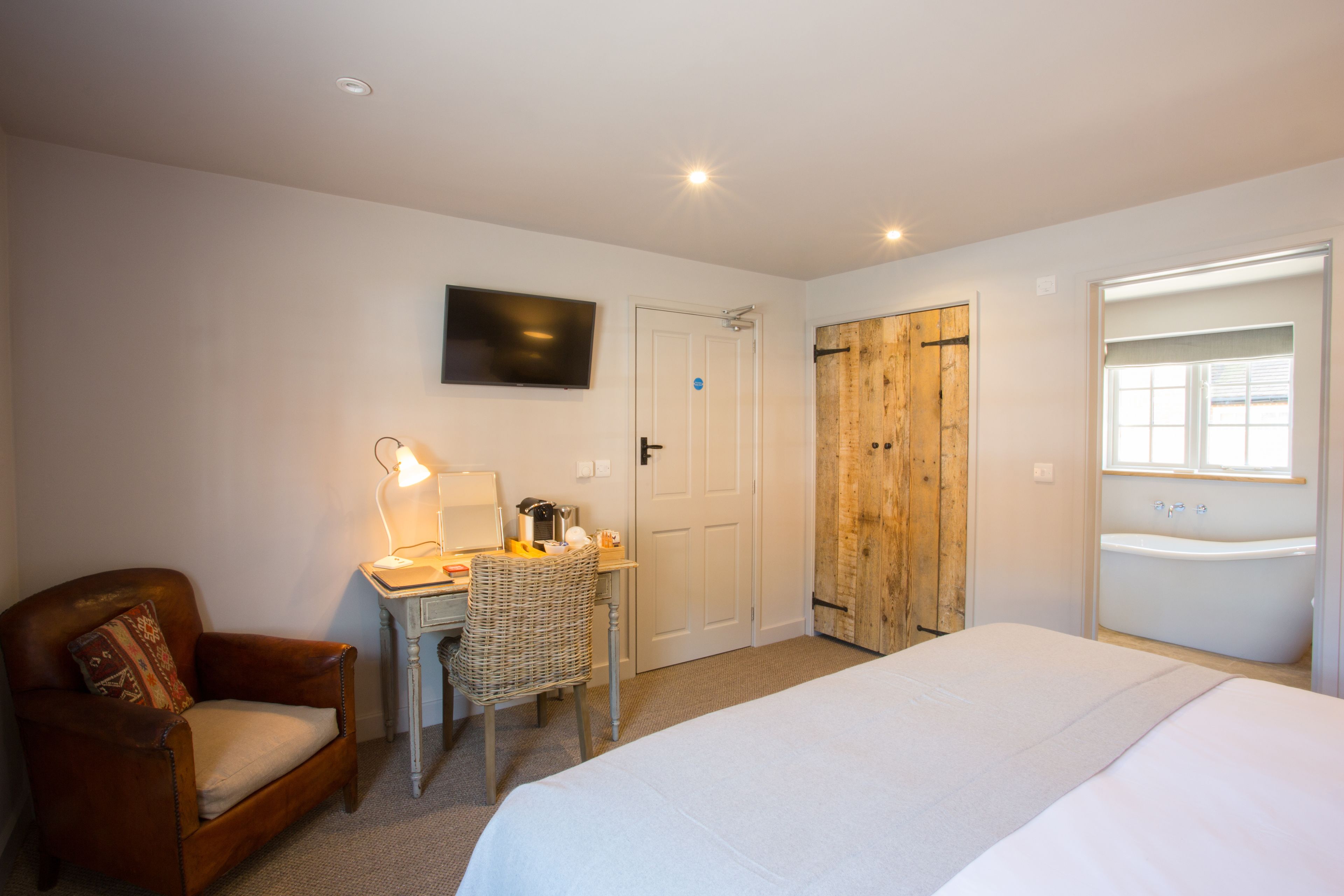 Quarto com cama, escrivaninha com luminária, cadeira, armário de madeira e banheiro com banheira.