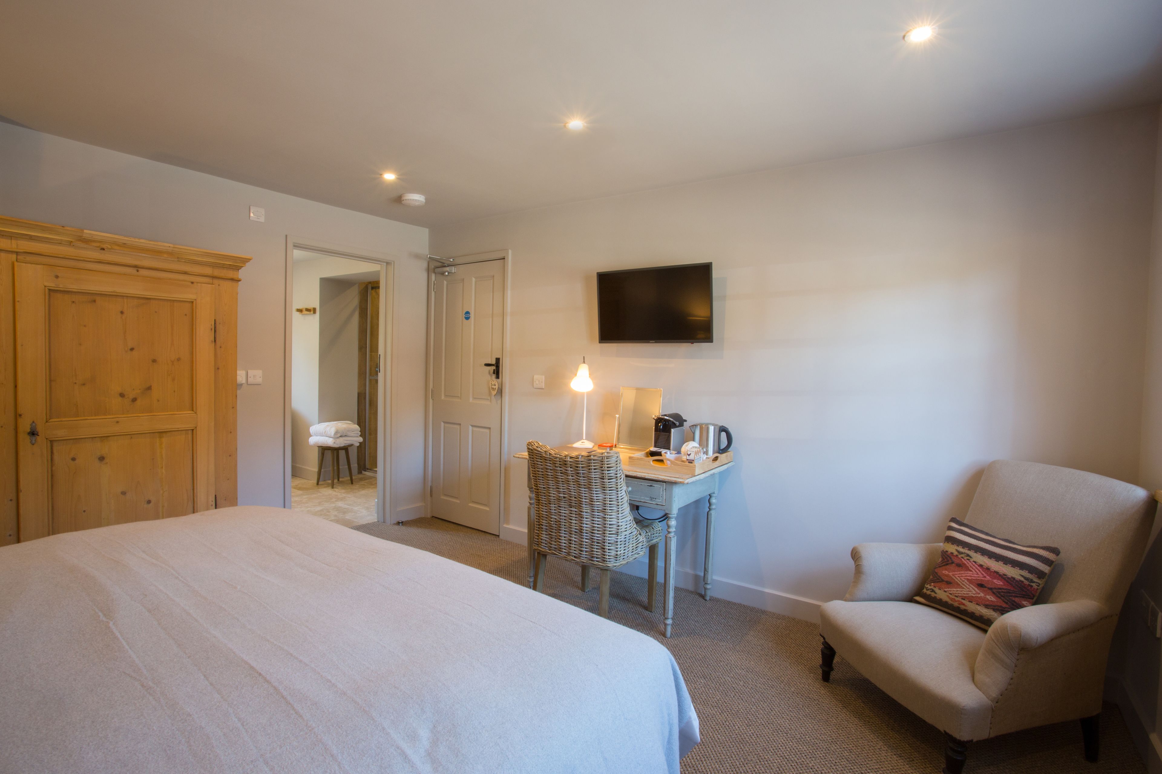 Een hotelkamer met een groot bed, een bureau met een lamp, een stoel en een televisie aan de muur.