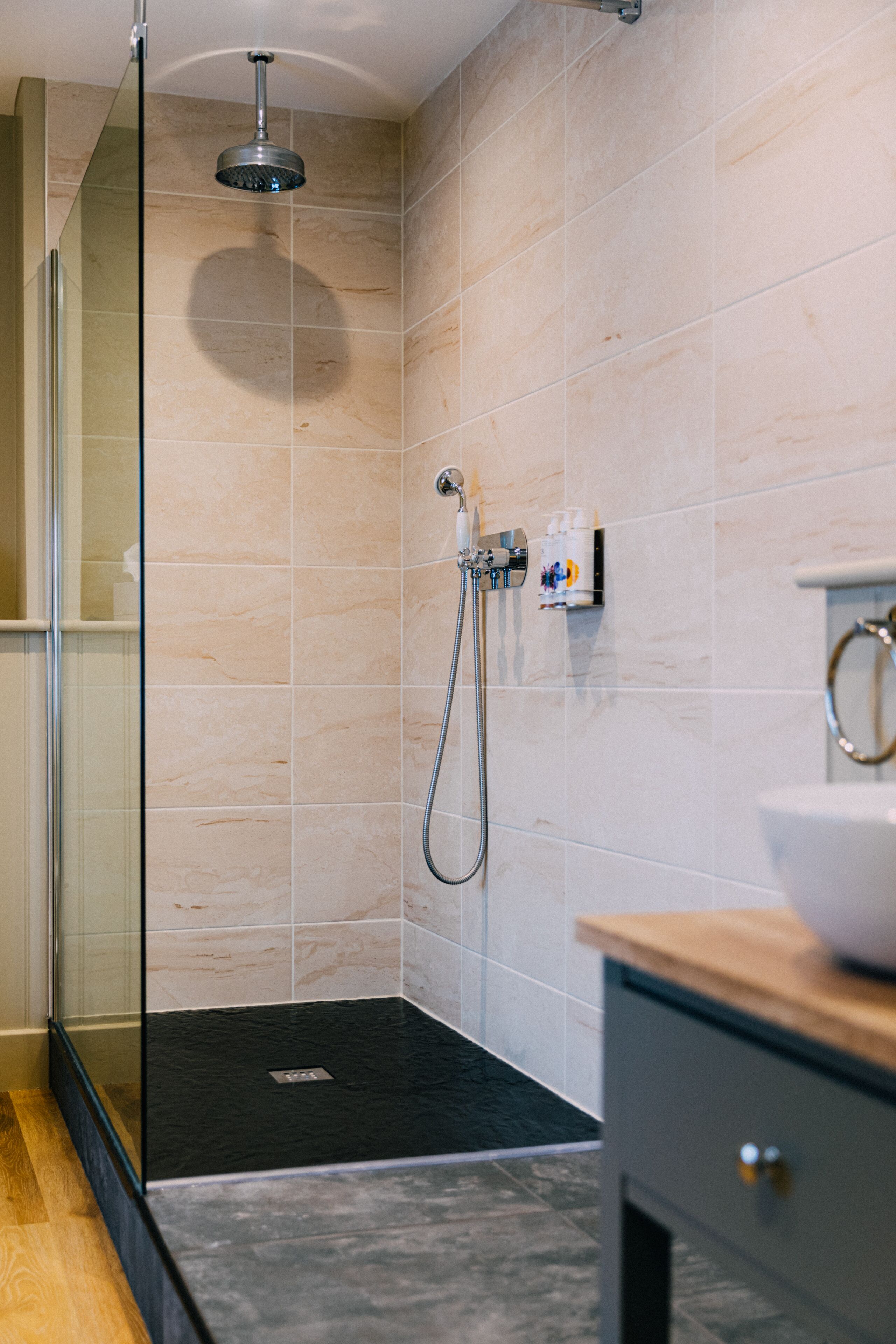 A modern bathroom with a glass shower enclosure, a black marble floor, and a wooden vanity with a sink.