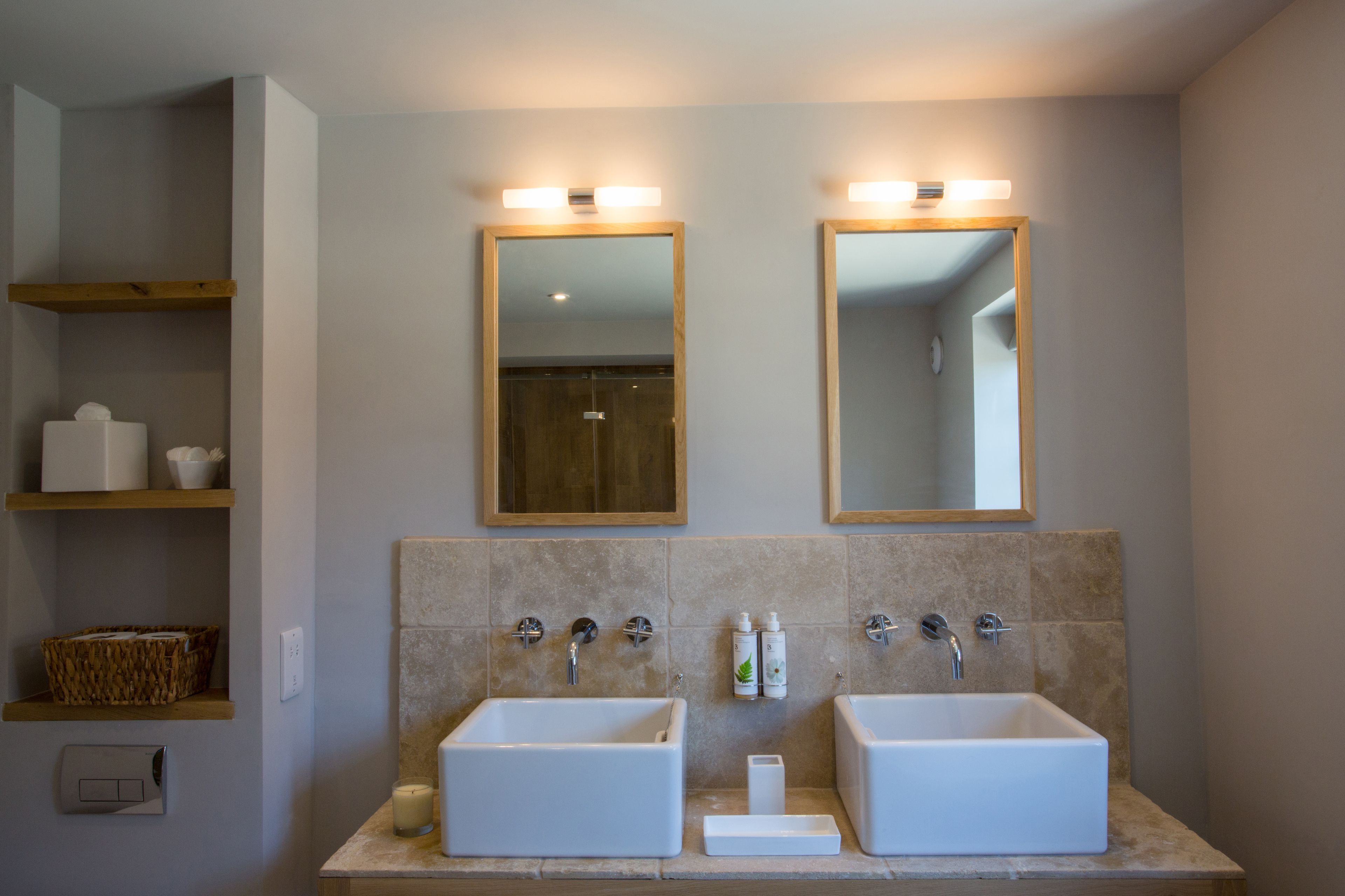 A bathroom with two sinks, a mirror above each, and shelves with toiletries.