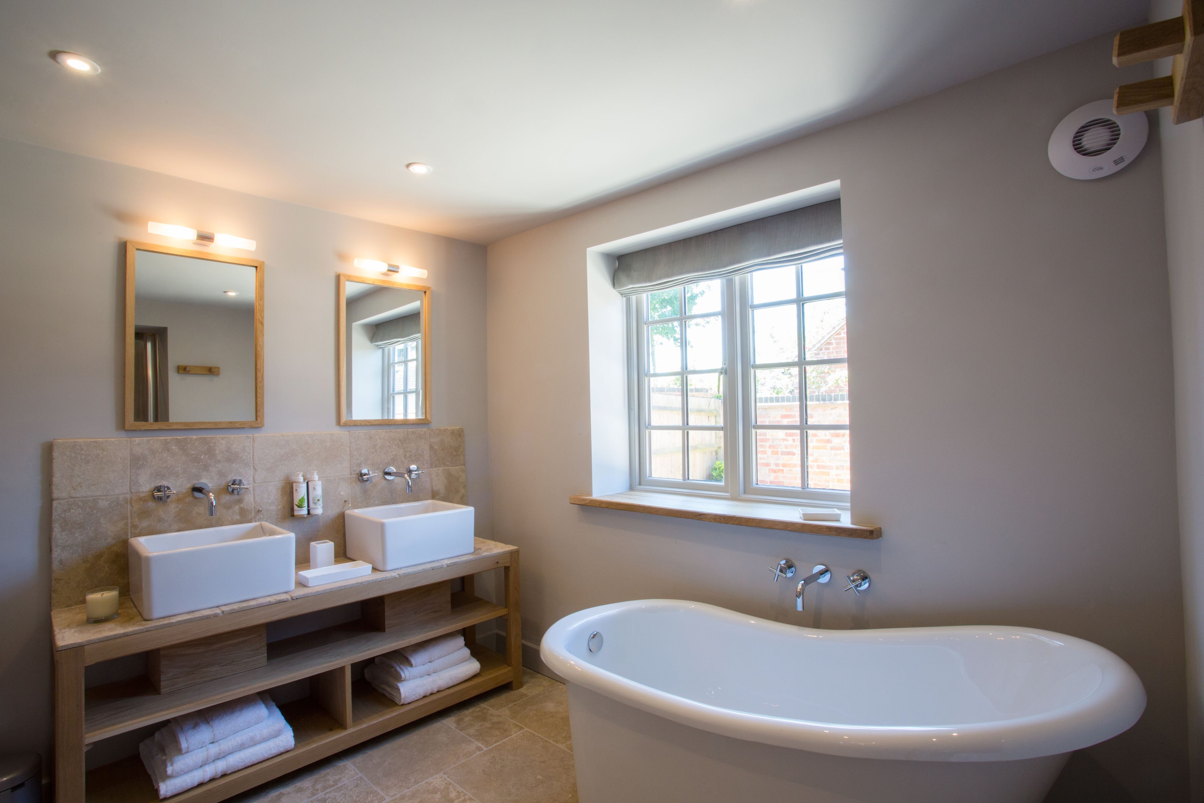 Ein modernes Badezimmer mit zwei Waschbecken, einer Badewanne und einem Fenster mit Tageslicht.