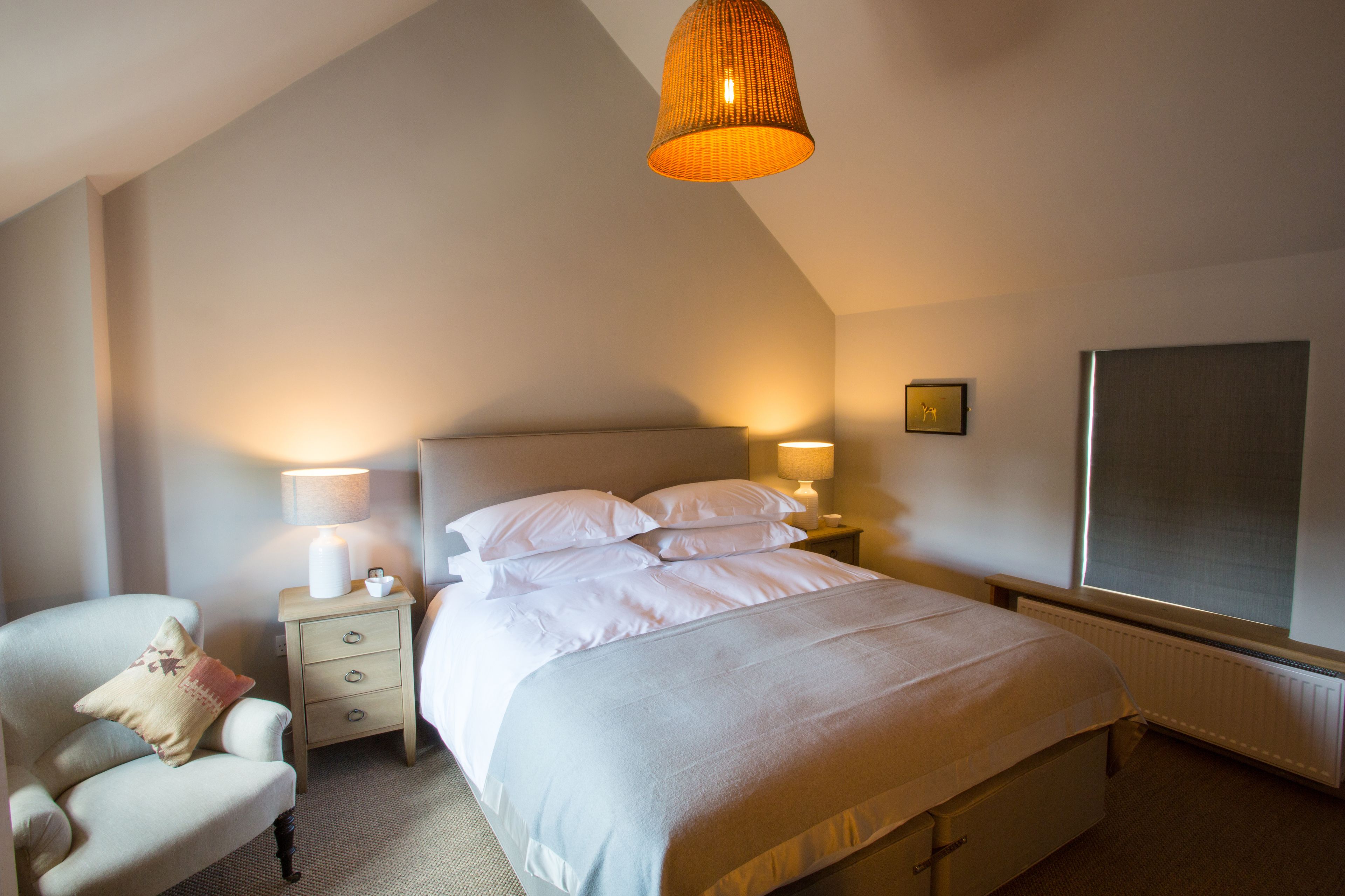 A neatly arranged bedroom with a bed, bedside lamps, a chair, and a large window.