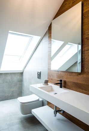 A modern bathroom with a skylight, a white sink, and a wooden accent wall.