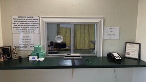 Een receptiebalie met een bericht voor gasten, een telefoon en een inlijsting met een onderscheiding aan de muur.