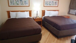 Een hotelkamer met twee bedden, houten hoofdborden, een nachtkastje met een lamp en ingelijste foto's aan de muur.