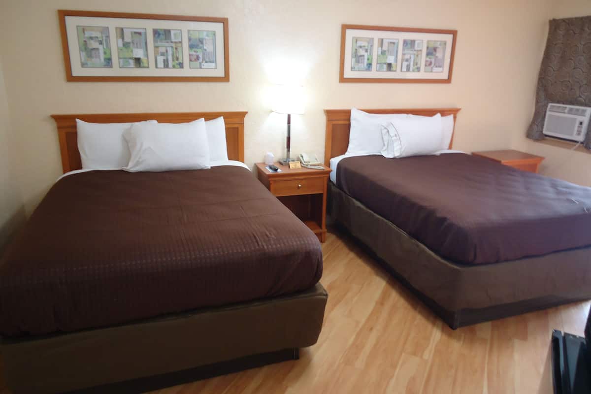 A hotel room with two beds, wooden headboards, a nightstand with a lamp, and framed pictures on the wall.