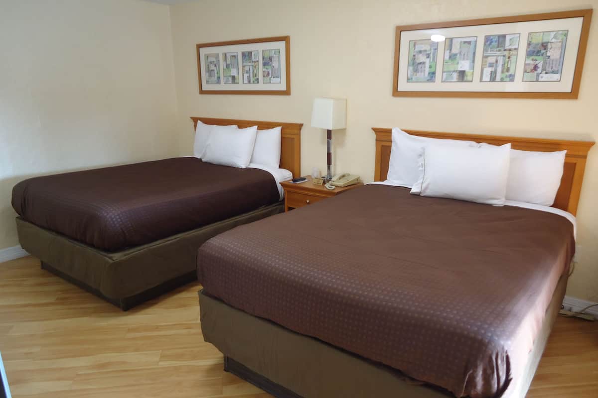 A hotel room with two beds, wooden headboards, and a nightstand with a lamp and phone.