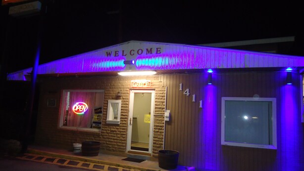 Een klein gebouw met een 'Welcome'-bord, een neon 'Open'-bord en een 'Visa'-bord.