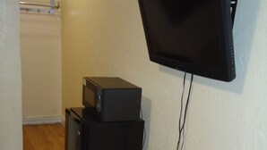 Een kamer met een wandgemonteerde flatscreen televisie, een kleine zwarte speaker en een stekkerdoos op de vloer.