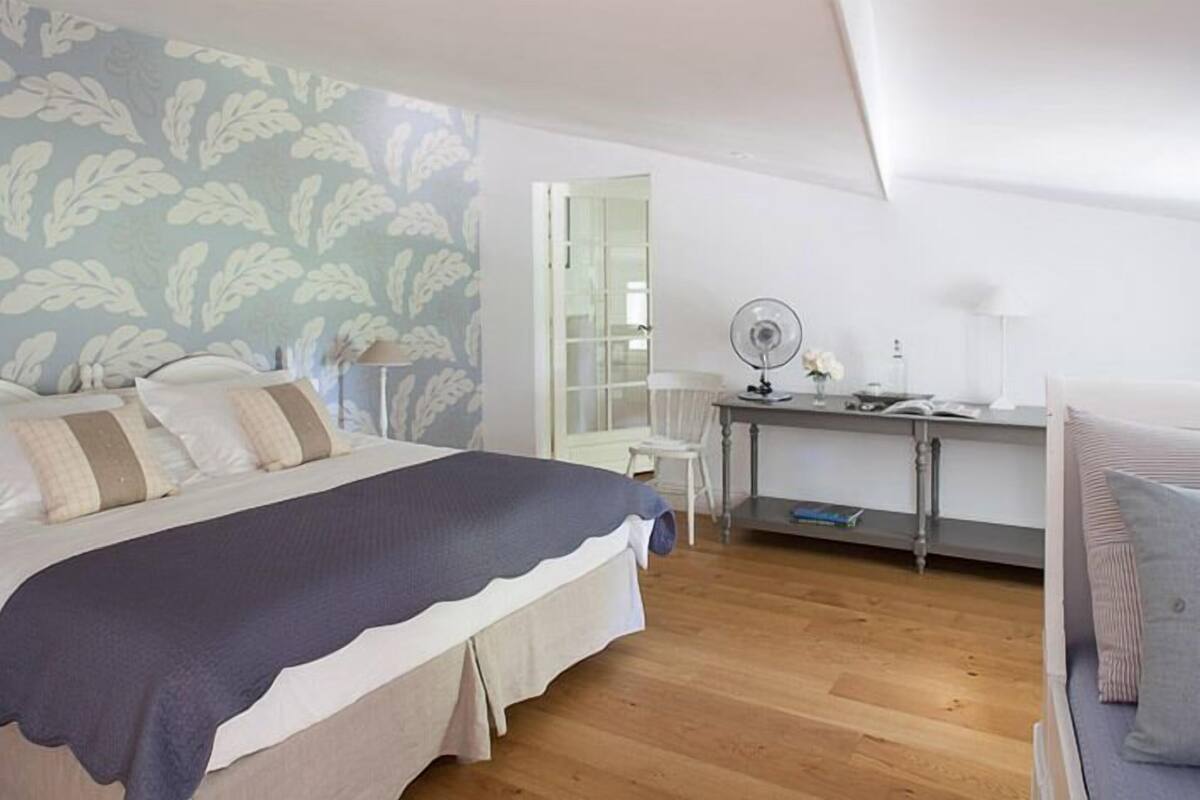A bedroom with a bed, a desk, a chair, and a bedside table.