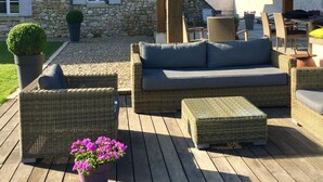 A stone building with a covered outdoor seating area featuring wicker furniture and a potted plant. - La Girarde (Saint-Quentin-de-Caplong)