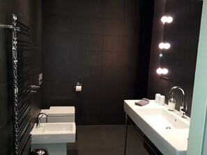 A modern bathroom with a black tiled wall, a white sink, and a mirror with lights. - urlaubsart - Schleibrücke (Kappeln)