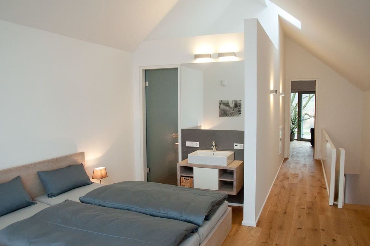 Quarto moderno com uma cama grande, mesa de cabeceira, espelho e pia embutida.