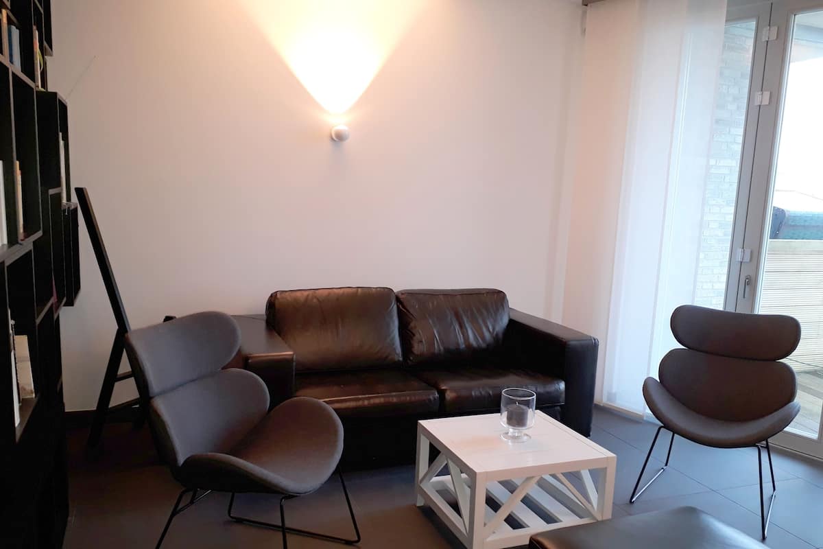 Uma sala de estar moderna com um sofá de couro, duas poltronas, uma mesa de centro e uma estante.