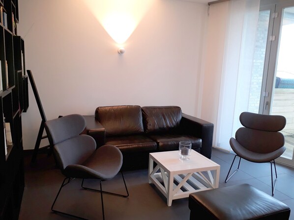 A modern living room with a leather sofa, two armchairs, a coffee table, and a bookshelf. - urlaubsart - Schleibrücke (Kappeln)