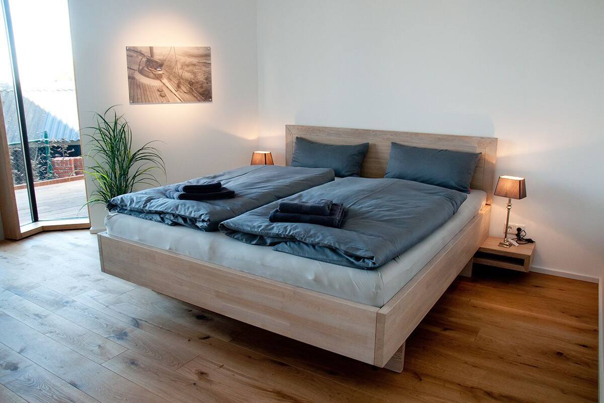 Quarto moderno com cama de madeira, duas mesas de cabeceira e uma janela grande.